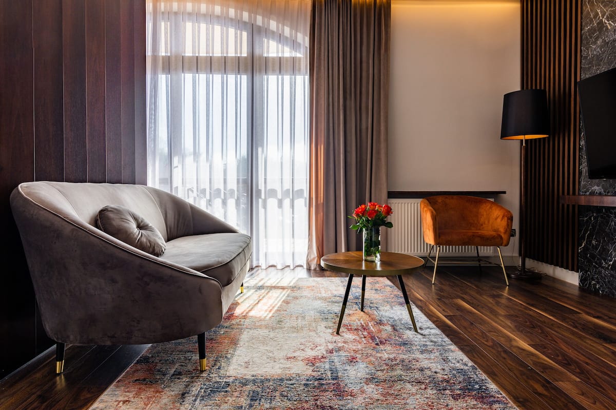 Een moderne woonkamer met een grijze bank, een klein rond tafeltje met een vaas rode bloemen, en een houten vloer.