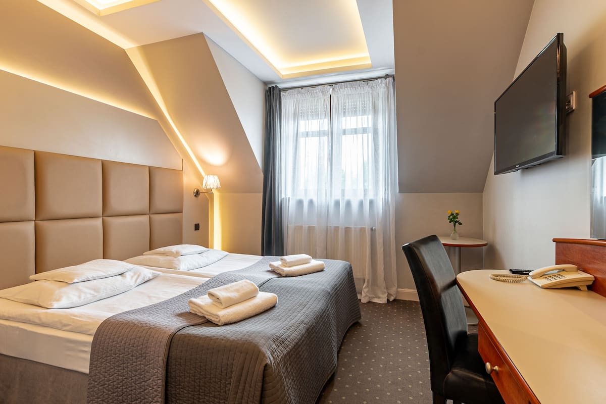 Een hotelkamer met twee bedden, een bureau, een stoel, een televisie en een raam met gordijnen.
