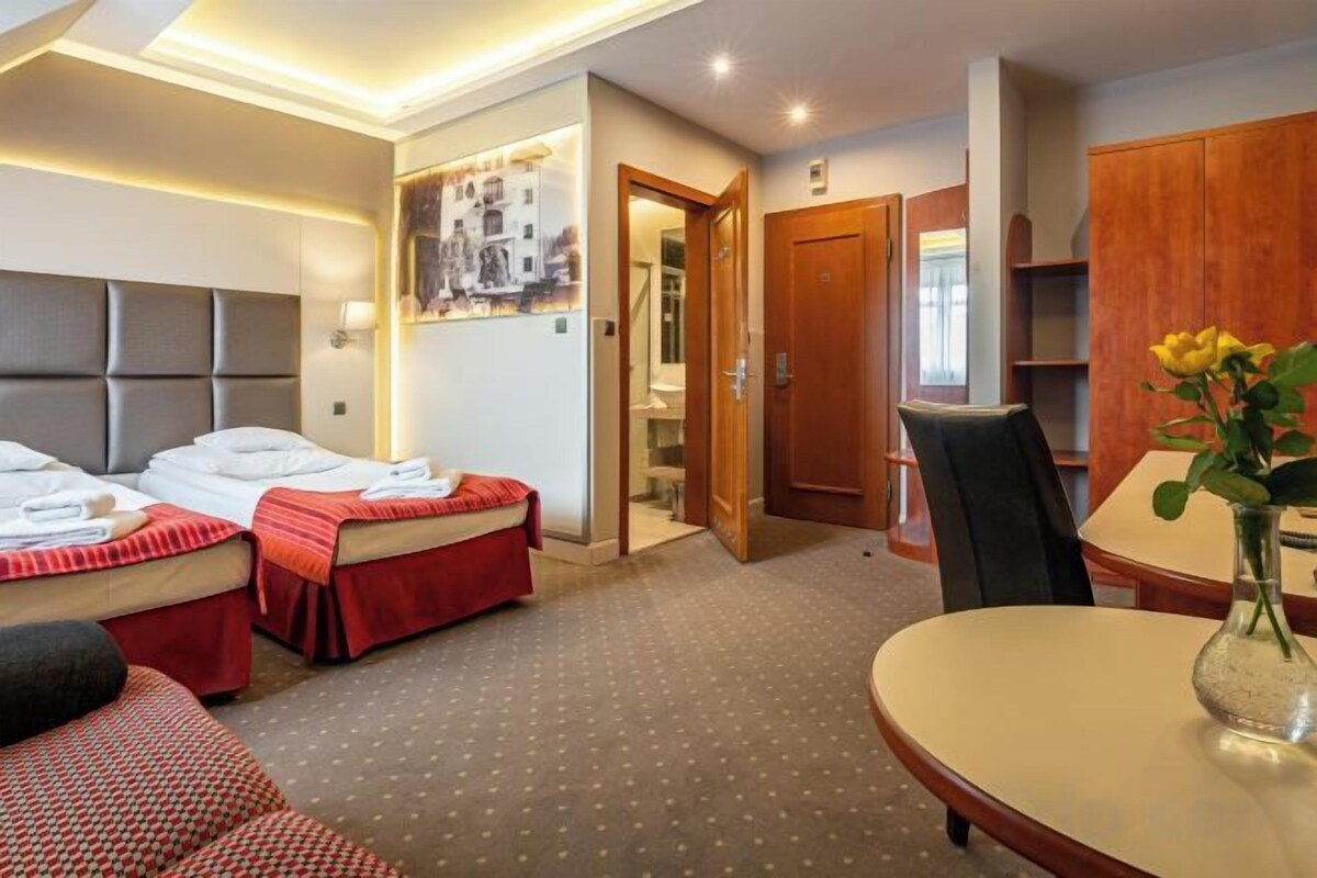 Ein Hotelzimmer mit zwei Betten, einem Esstisch, einem Stuhl und einem kleinen Tisch mit einer Vase.