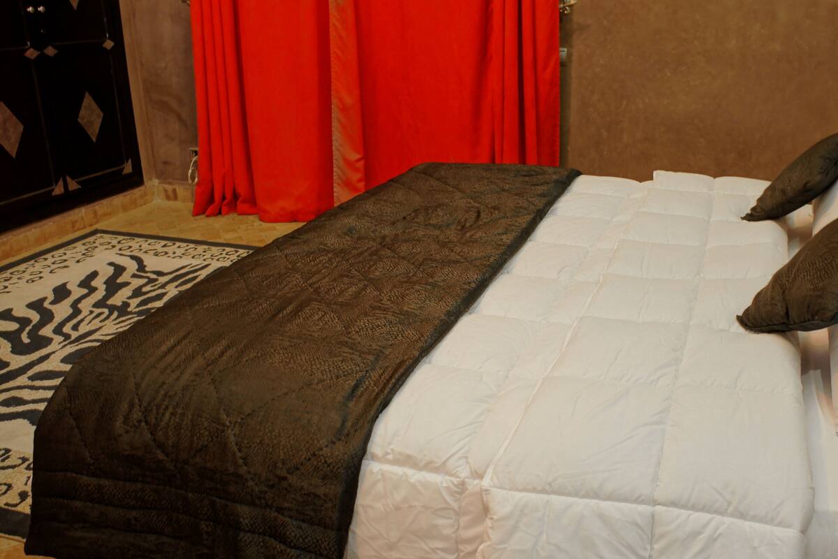 A bed with a white and brown quilt, two pillows, and a zebra-patterned rug.