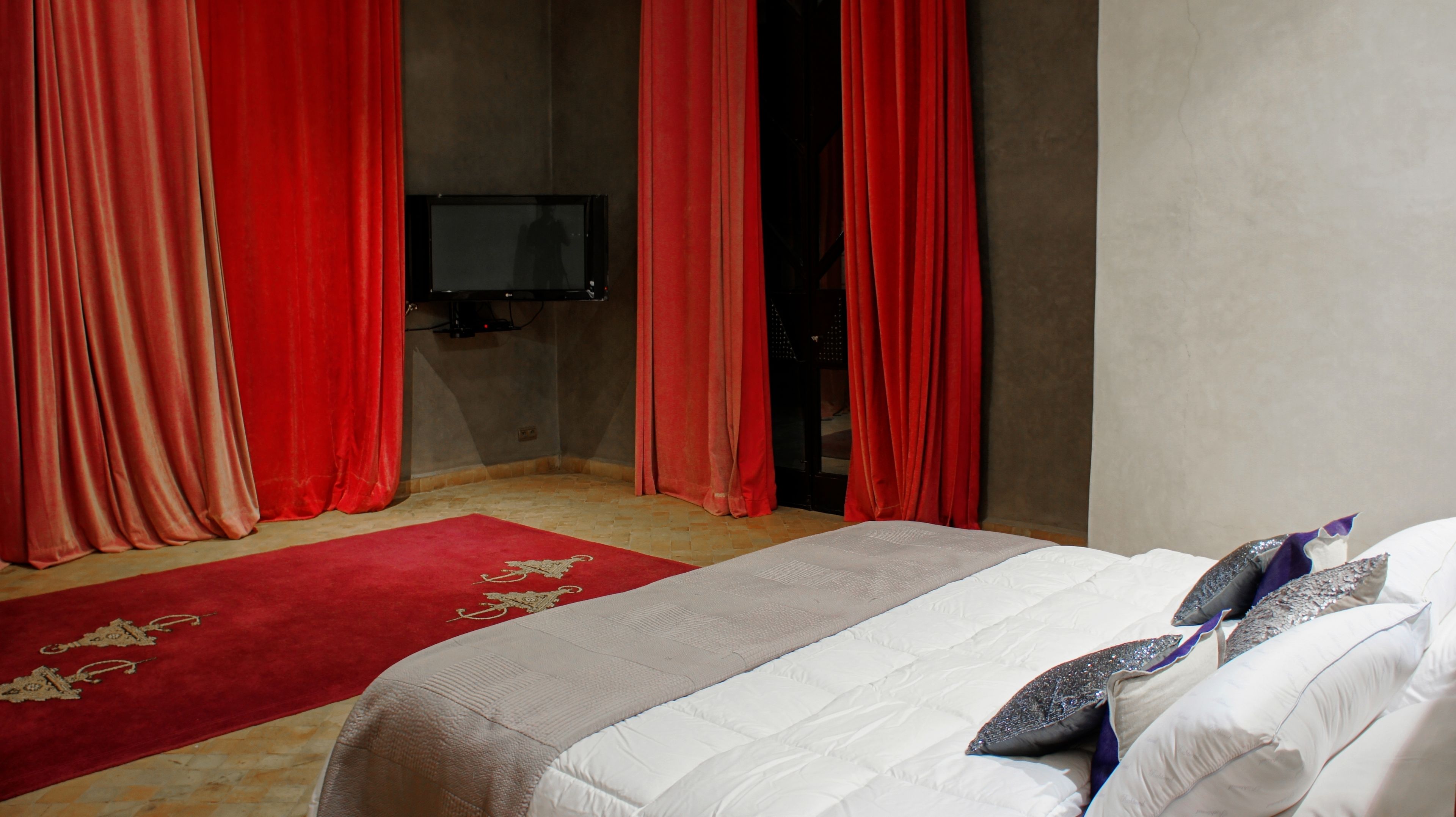 Une chambre d’hôtel avec un lit, des rideaux rouges, une télévision et une moquette rouge.