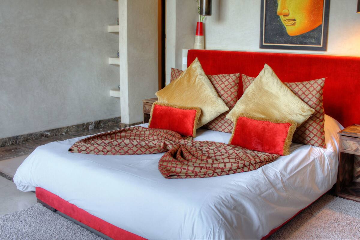 A bed with a red headboard, multiple pillows, and a patterned bedspread.