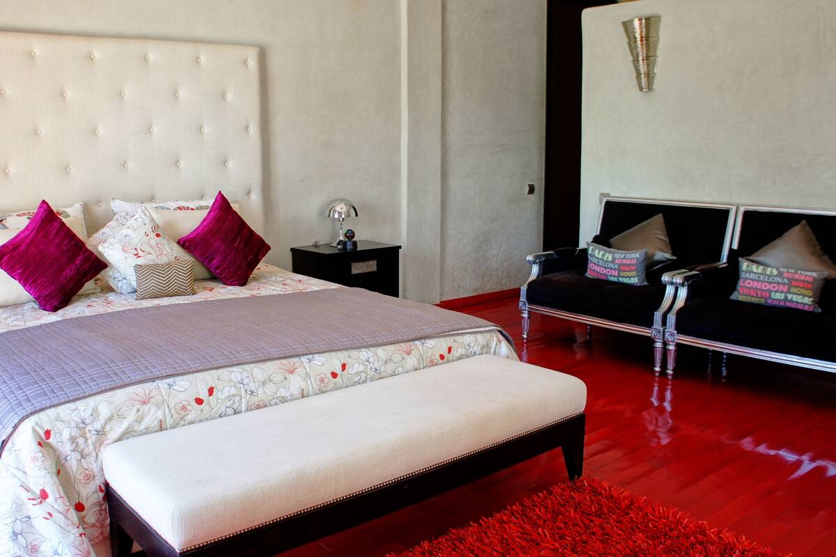 A bedroom with a large bed, a bedside table, a nightstand, a chair, and a red rug.