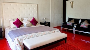 A bedroom with a large bed, a bedside table, a nightstand, a chair, and a red rug. - Maradisse Bhakti Villas (Marrakech)