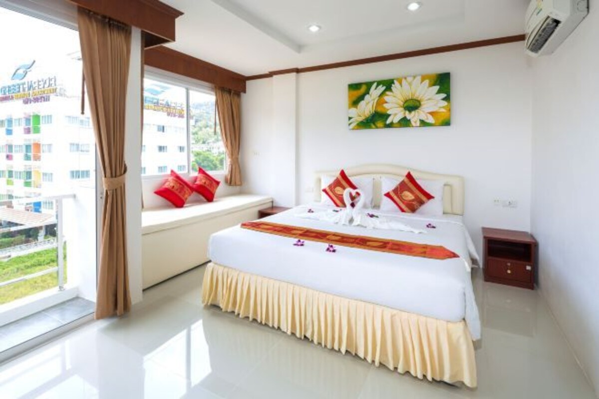 A hotel room with a large bed, a window with curtains, a small bedside table, and a wall-mounted air conditioner.