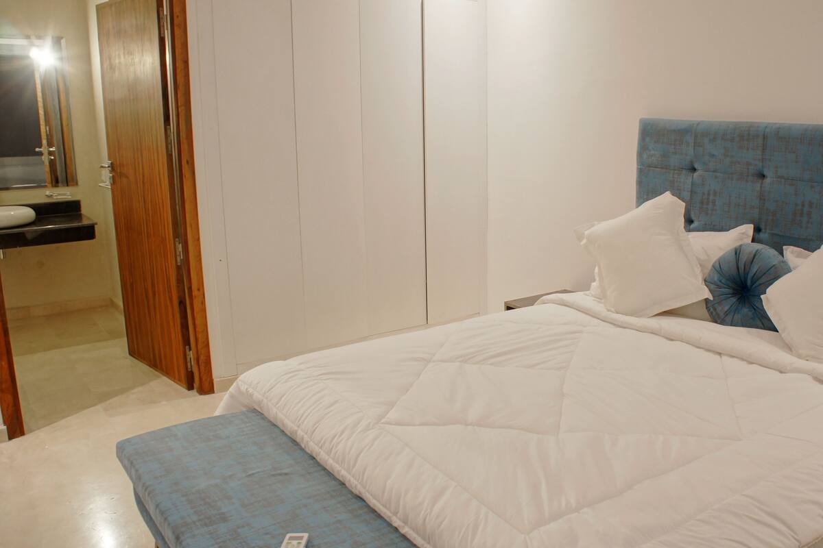 A bedroom with a bed, pillows, a nightstand, and a wooden wardrobe.