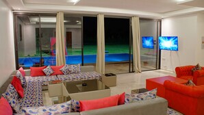 A modern living room with a sofa set, a red armchair, and a glass door leading to a pool area. - Plage Rouge Luxury Villas (Marrakech)