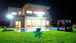 Ein modernes, zweistöckiges Haus mit Schwimmbad, Außenbereich zum Sitzen und einer überdachten Spielzone.