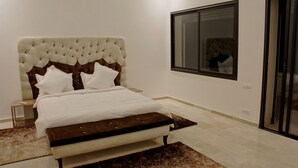 A bedroom with a tufted headboard, a large bed with white bedding, a wooden bench, and a view of the outside through a window. - Plage Rouge Luxury Villas (Marrakech)
