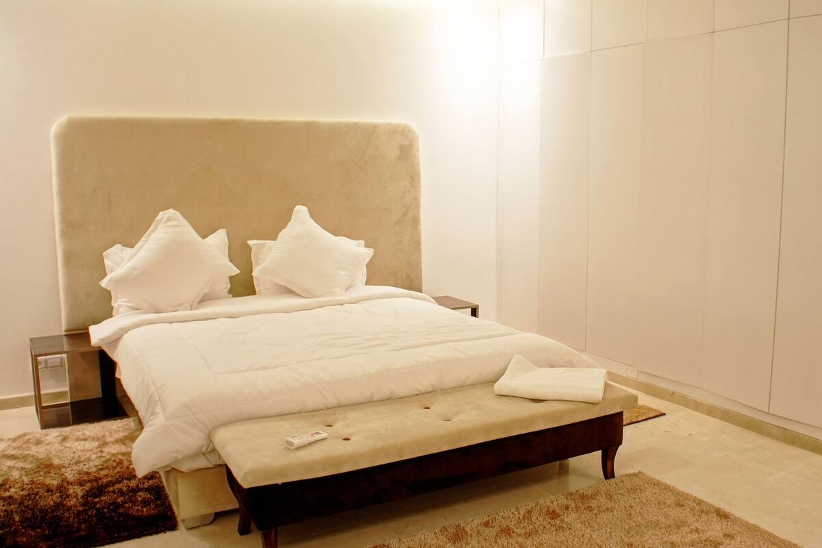A neatly made bed with a headboard, a bedside table, and a bench at the foot of the bed.