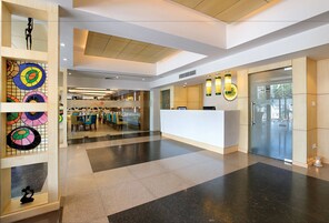 Un moderno vestíbulo de hotel con mostrador de recepción, zona de estar y paneles de vidrio decorativos.