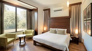 A hotel room with a large bed, two armchairs, a small table, and a nightstand with lamps.