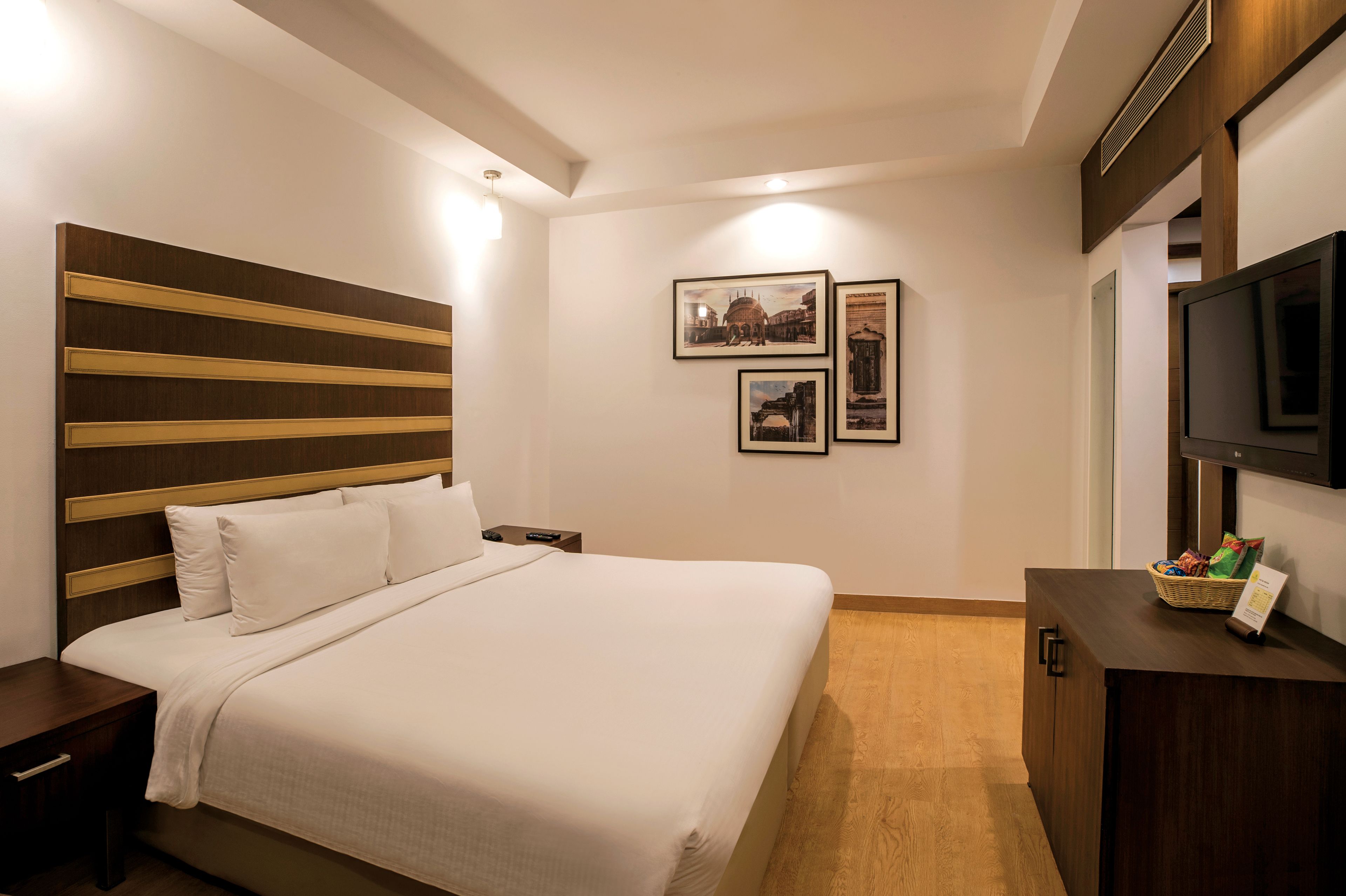 A neatly made bed with a wooden headboard, a small bedside table, and a television on a wooden cabinet.
