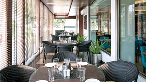 A restaurant with outdoor seating, including round tables and wicker chairs, and a potted plant on the table. - Lemon Tree Hotel Alwar (Alwar)