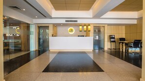 A modern reception area with a central desk, seating, and a decorative wall. - Lemon Tree Hotel Alwar (Alwar)
