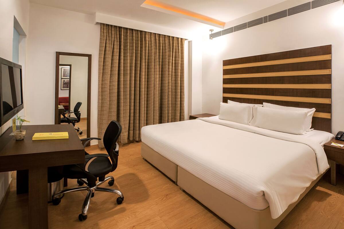 Habitación de hotel con una cama grande, un escritorio con silla, un televisor y una ventana con cortinas.