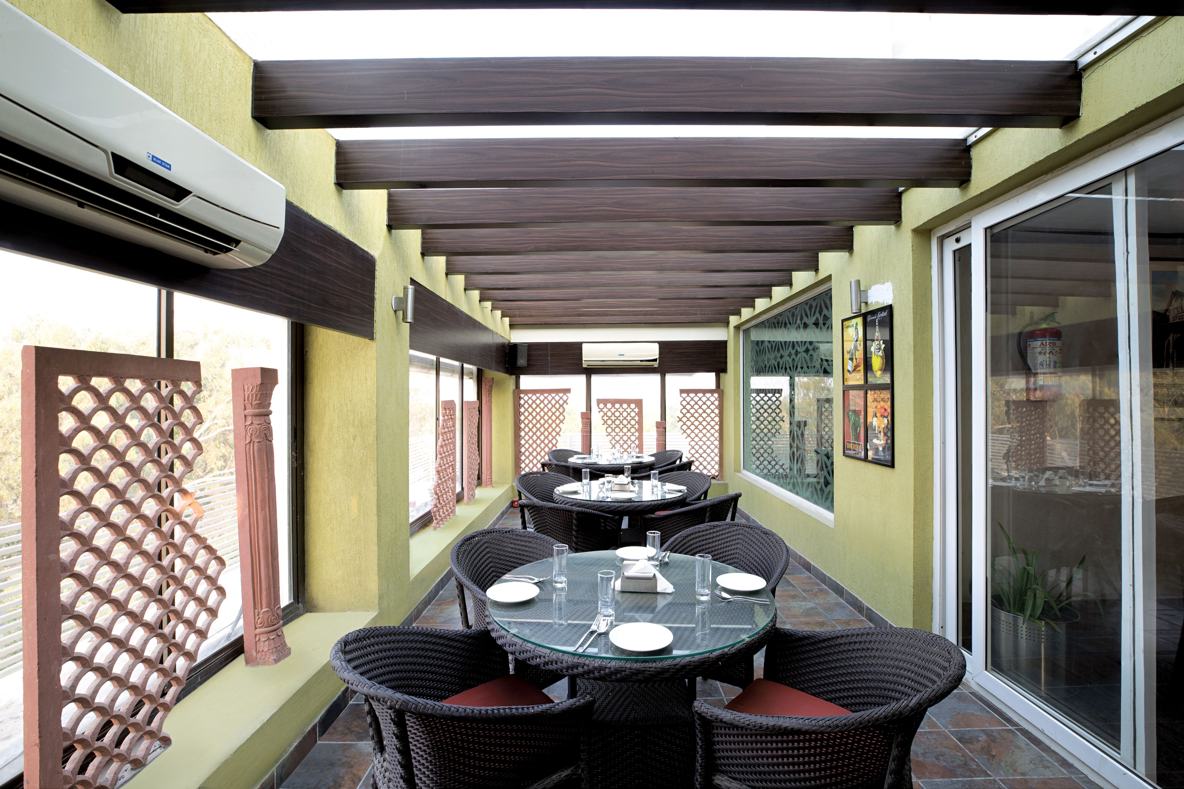 Un área de comedor al aire libre con varias mesas y sillas, aire acondicionado y vistas a través de un ventanal.