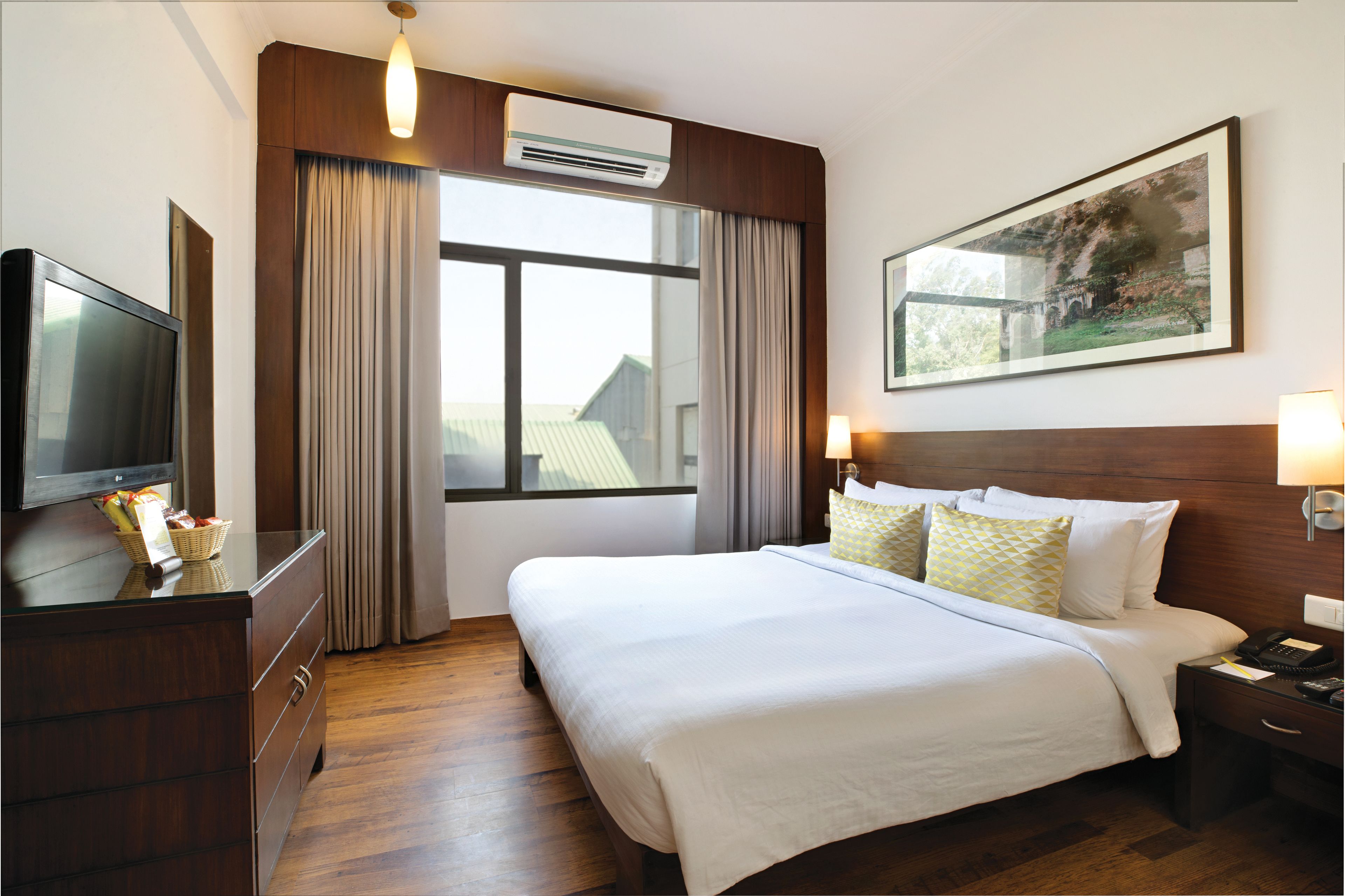 A hotel room with a large bed, a television on a dresser, a window with curtains, and a painting on the wall.