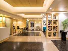 Um lobby moderno de hotel com balcão de recepção, área de estar e exposição de obras de arte na parede.
