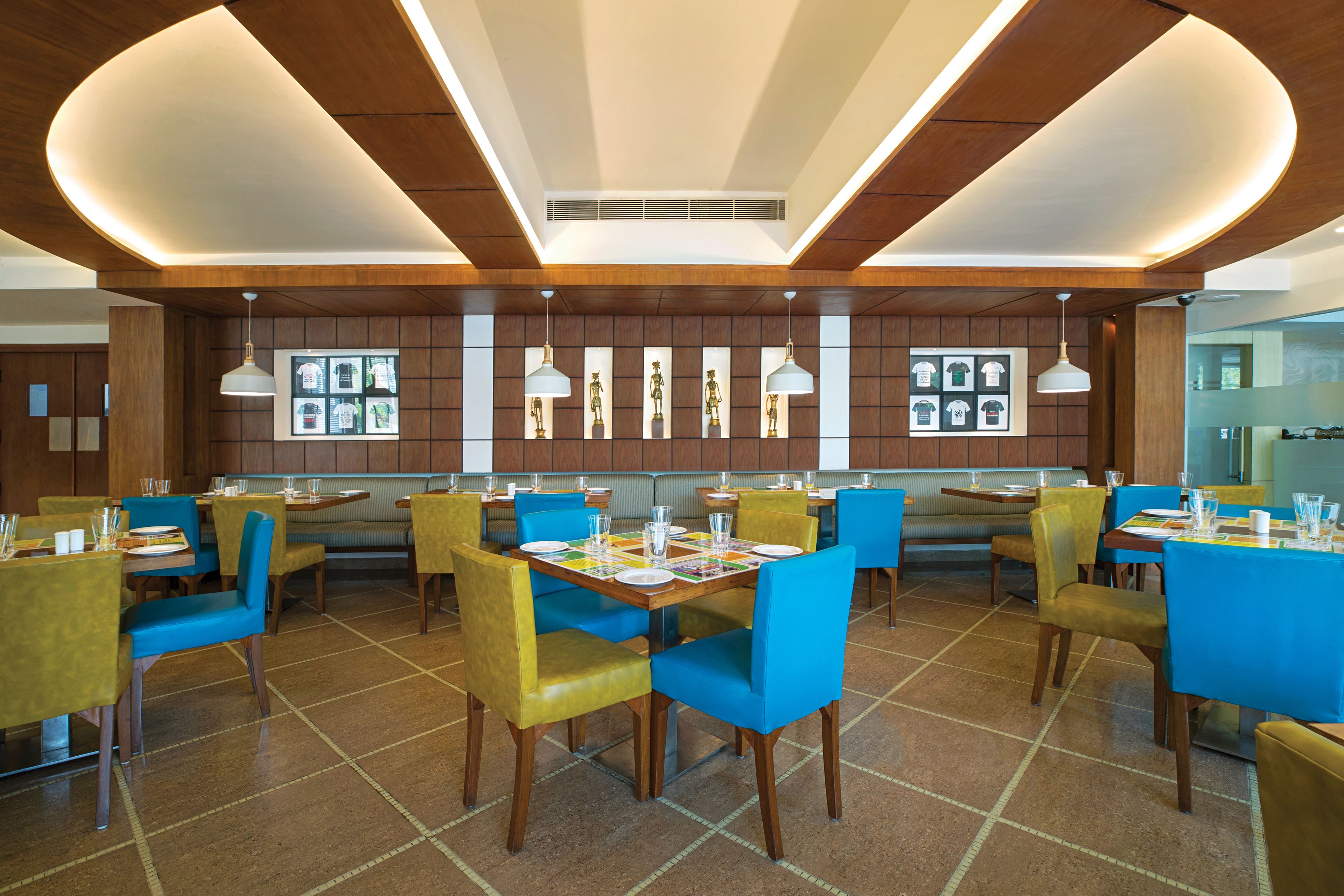 A modern restaurant with wooden panel walls, blue and yellow chairs, and white pendant lighting.