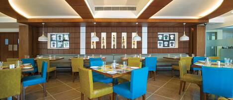 A modern restaurant with wooden panel walls, blue and yellow chairs, and white pendant lighting.