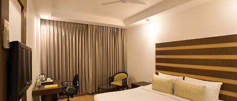 A hotel room with a bed, a desk, a chair, a television, and a ceiling fan.