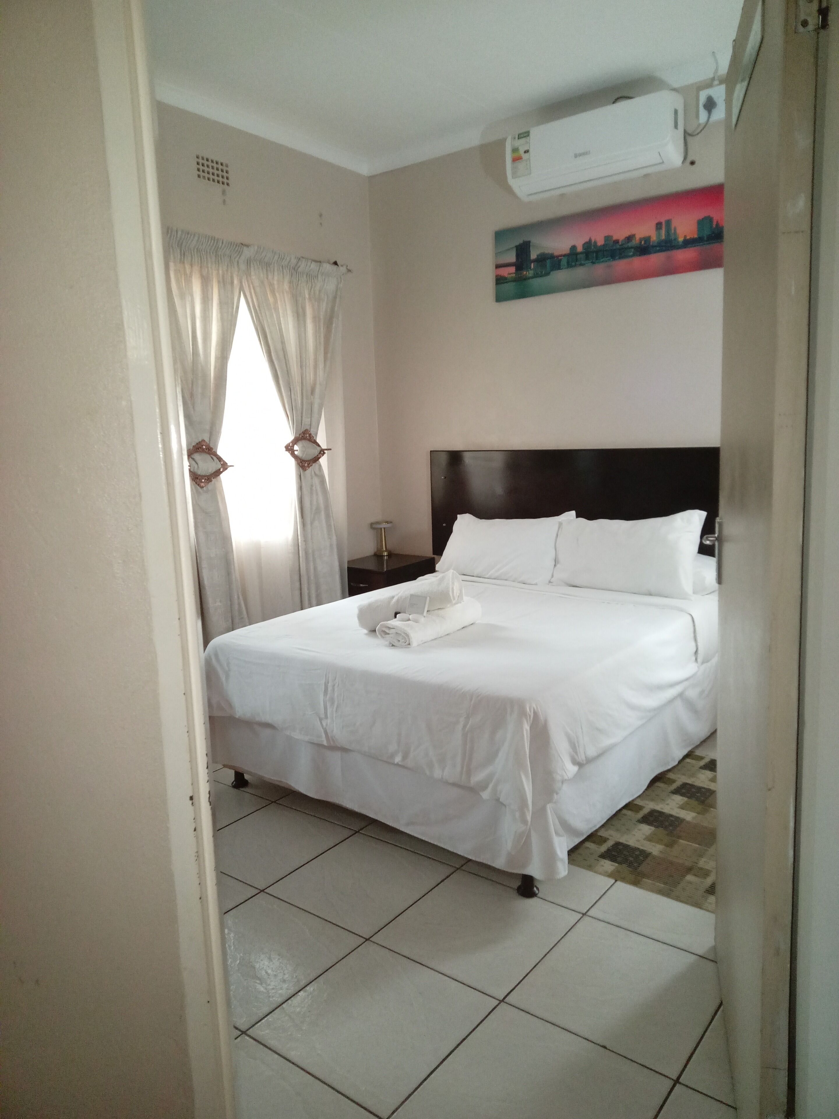 A hotel room with a bed, a nightstand, a lamp, and a painting on the wall.