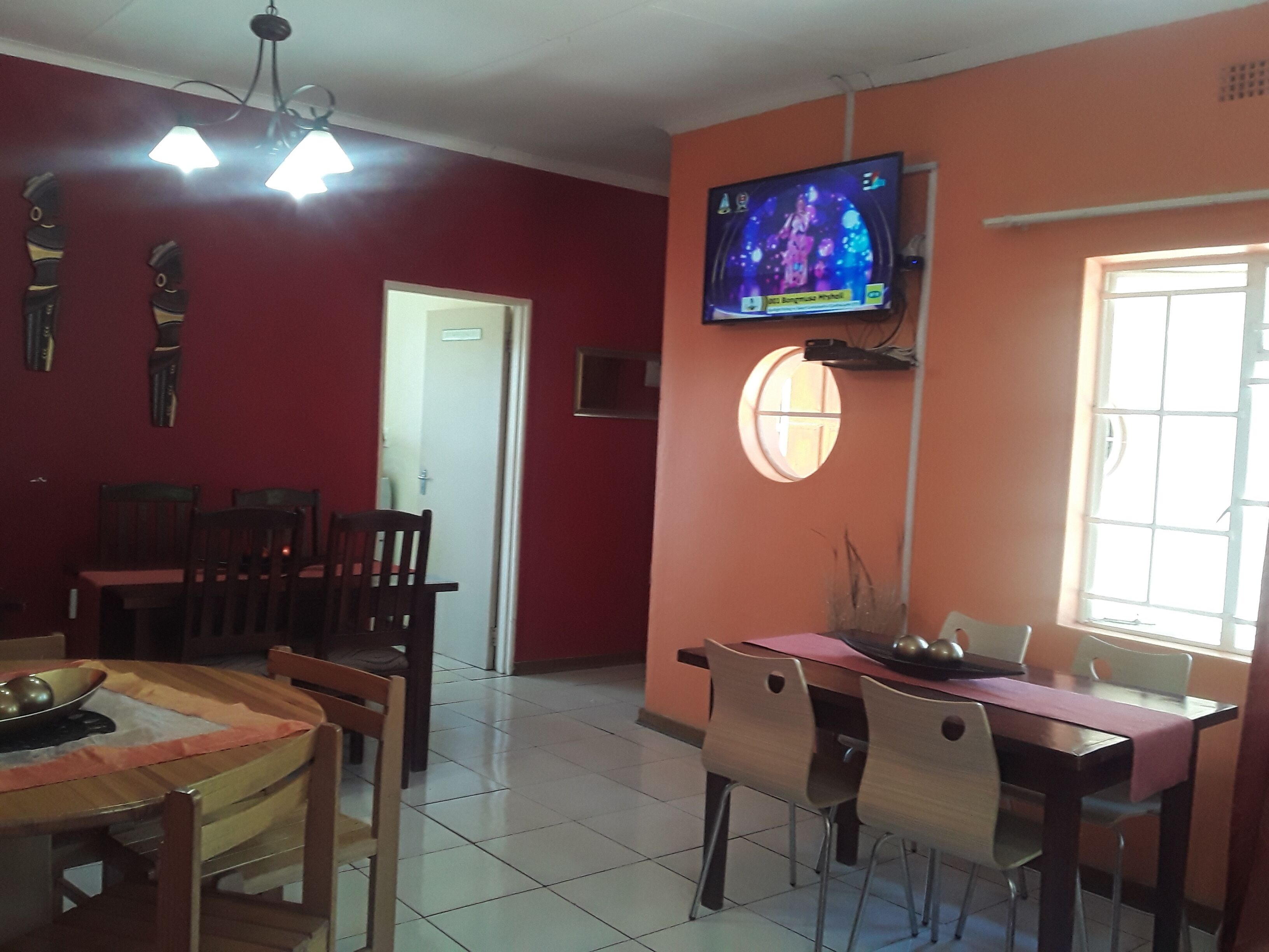 A dining area with a TV mounted on the wall, a window with a view, and a door leading to another room.