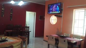 A dining area with a TV mounted on the wall, a window with a view, and a door leading to another room.