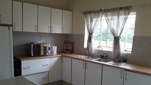 Una cocina con armarios blancos, microondas, cafetera y una ventana con cortinas.