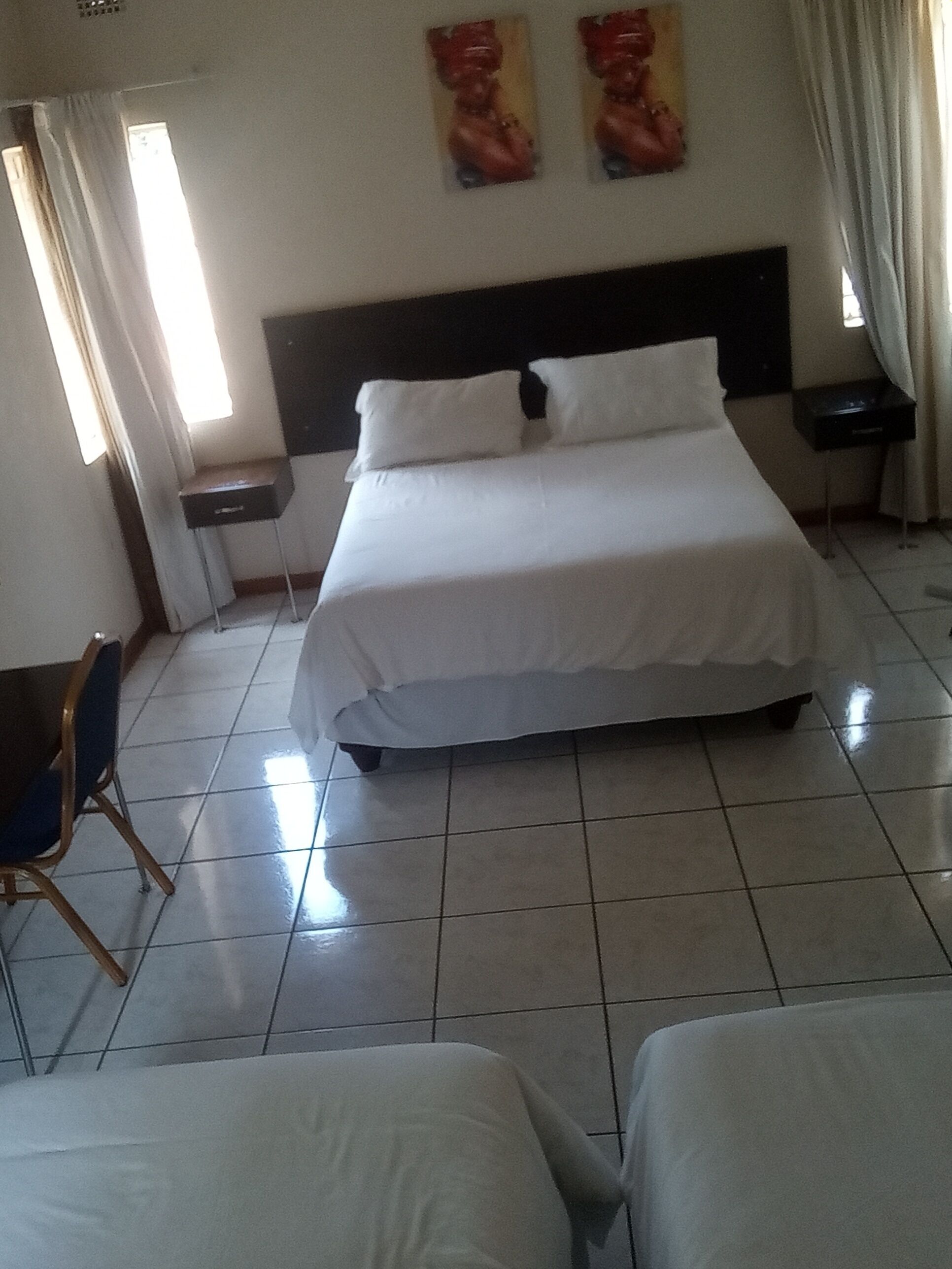 A hotel room with a bed, two nightstands, a chair, and a window with curtains.