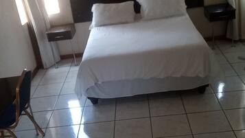 A hotel room with a bed, two nightstands, a chair, and a window with curtains.