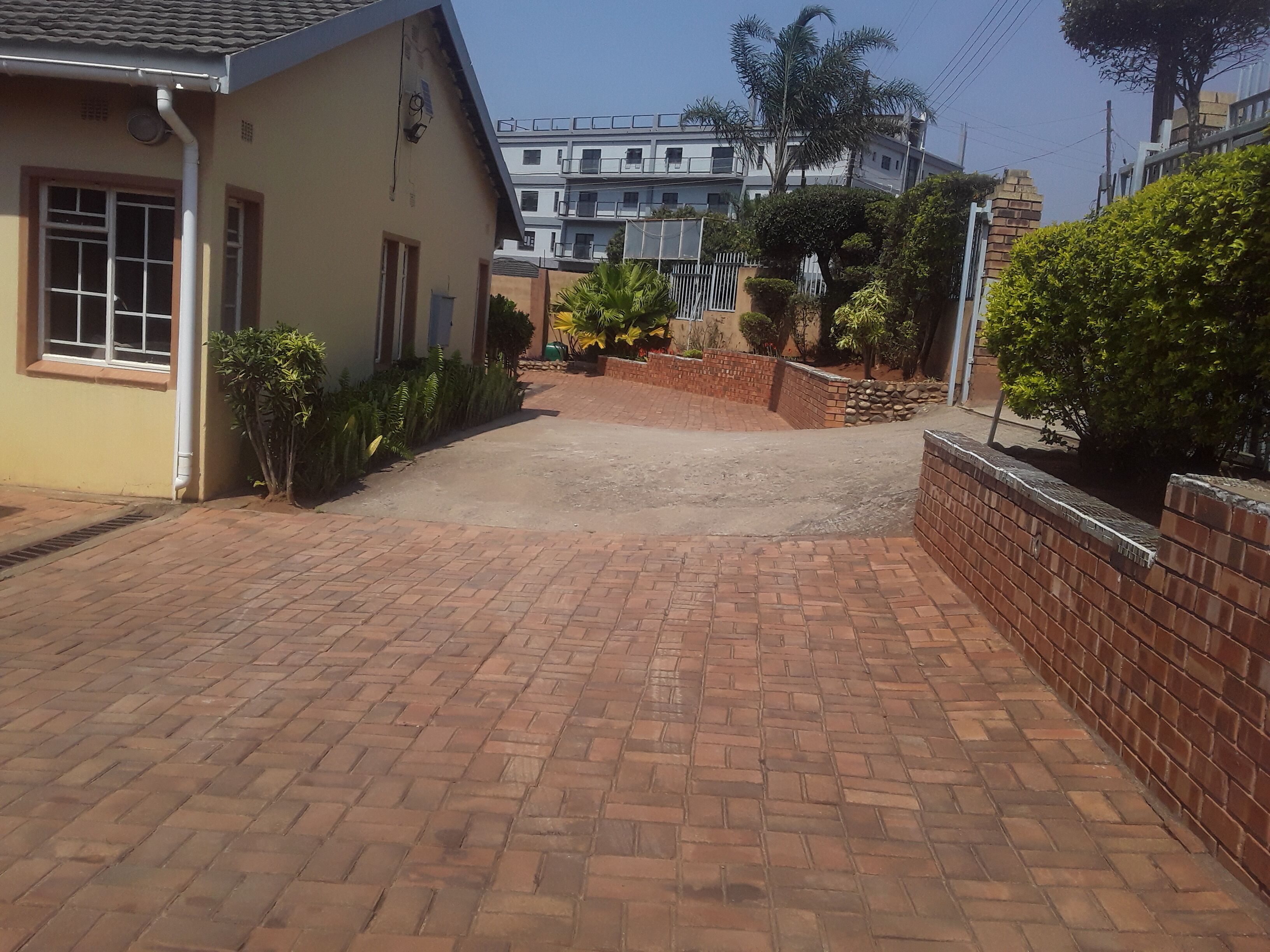 A paved driveway leading to a building with a brick wall and a small garden area.
