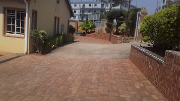 A paved driveway leading to a building with a brick wall and a small garden area.