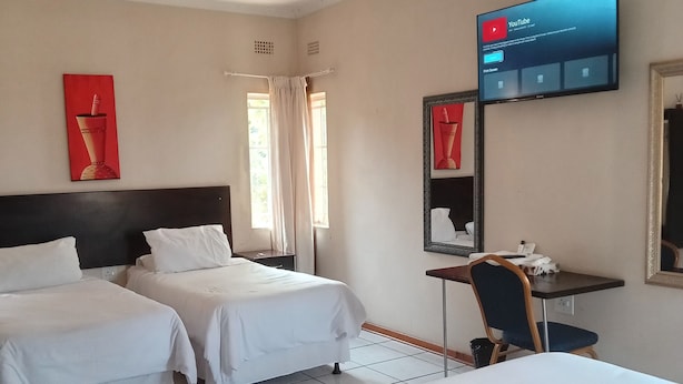 Habitación de hotel con dos camas, un escritorio, una silla, un televisor montado en la pared y una ventana con cortinas.
