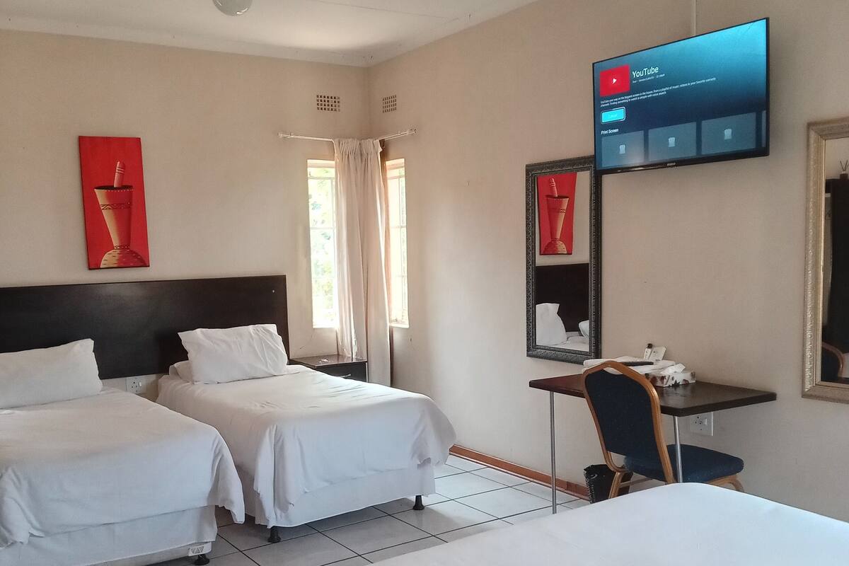 A hotel room with two beds, a desk, a chair, a TV mounted on the wall, and a window with curtains.