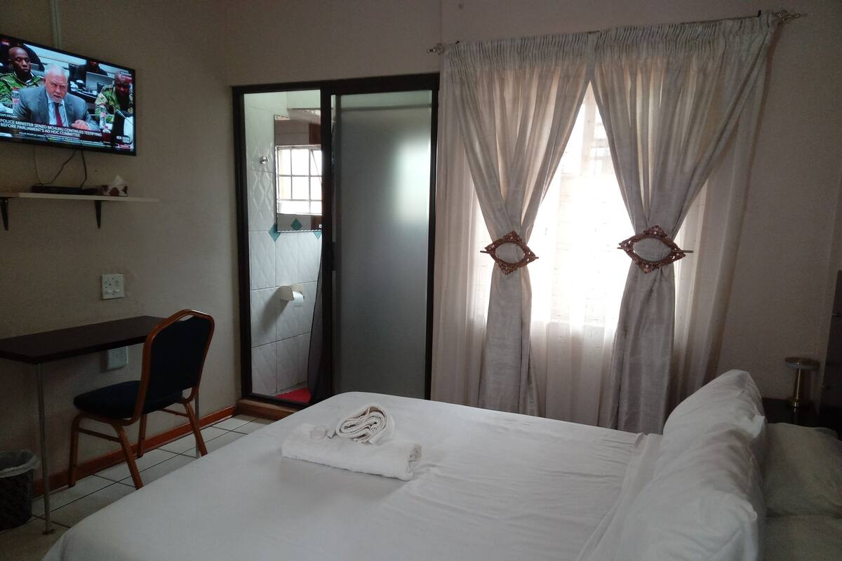 A hotel room with a bed, a desk, a chair, a TV, and a window with curtains.