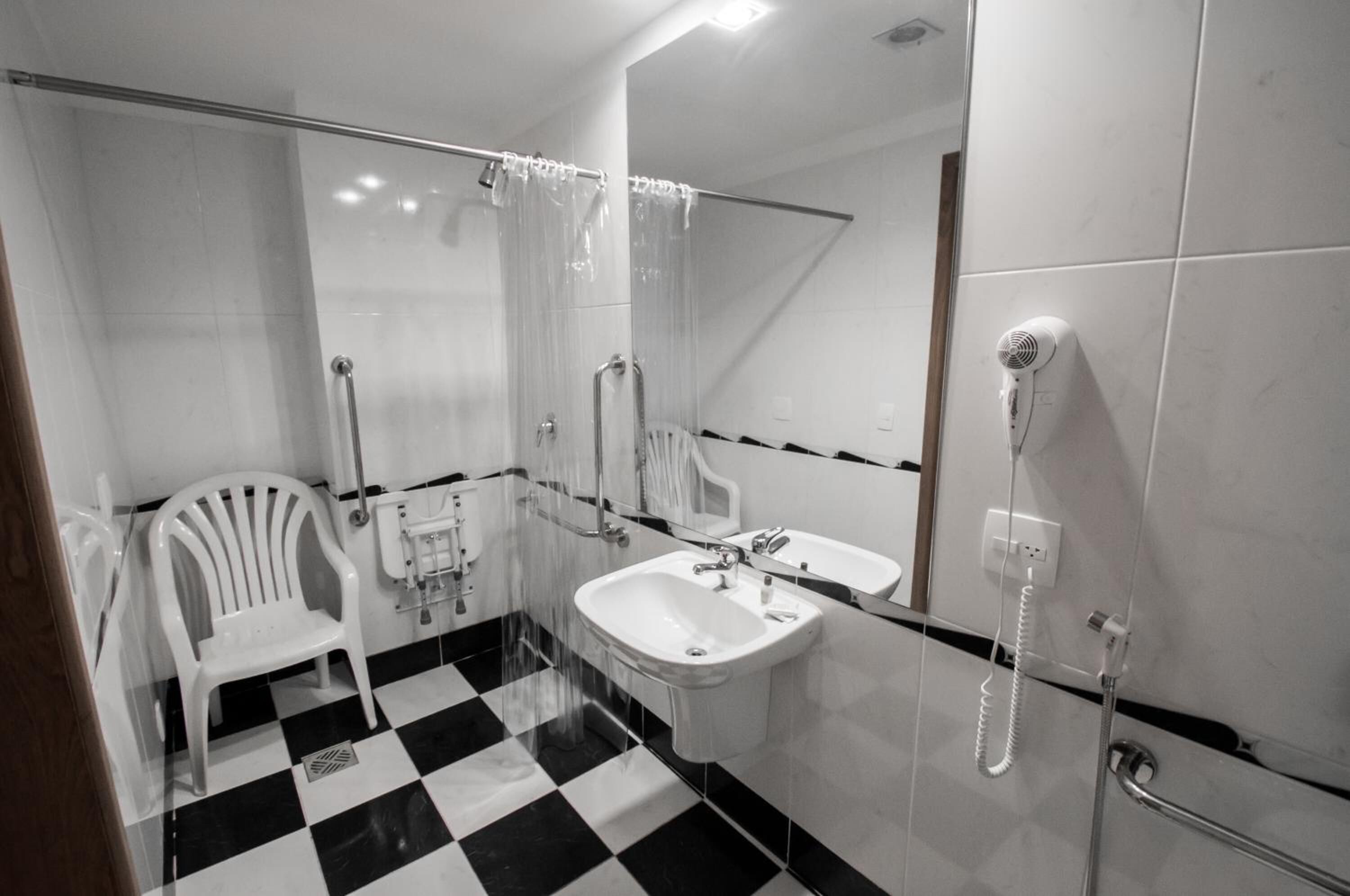 Un baño con piso a cuadros, un lavamanos blanco, un espejo, una ducha con puerta de vidrio y un secador de pelo.