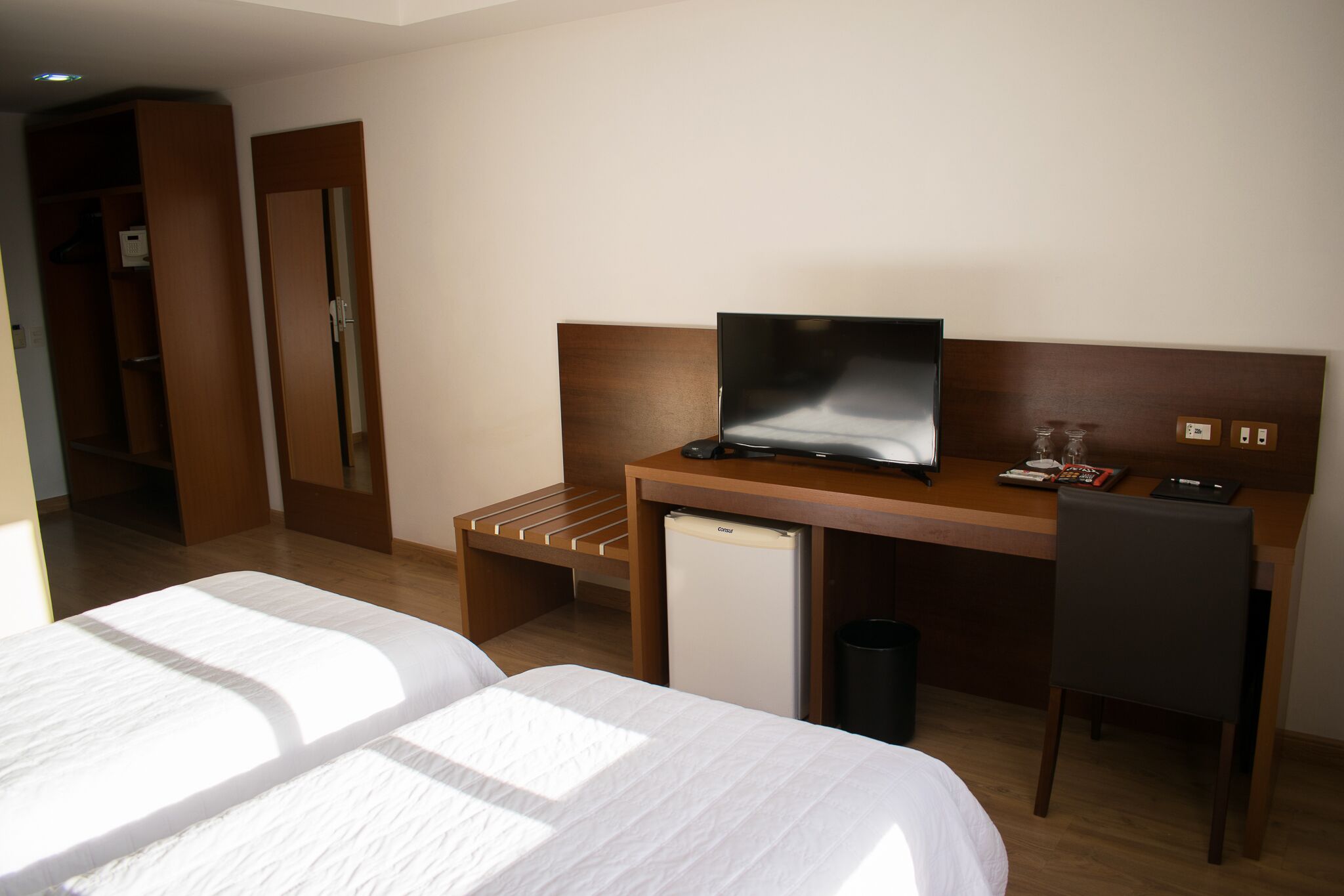 Habitación de hotel con dos camas, un escritorio con computadora, un mini refrigerador y una silla.