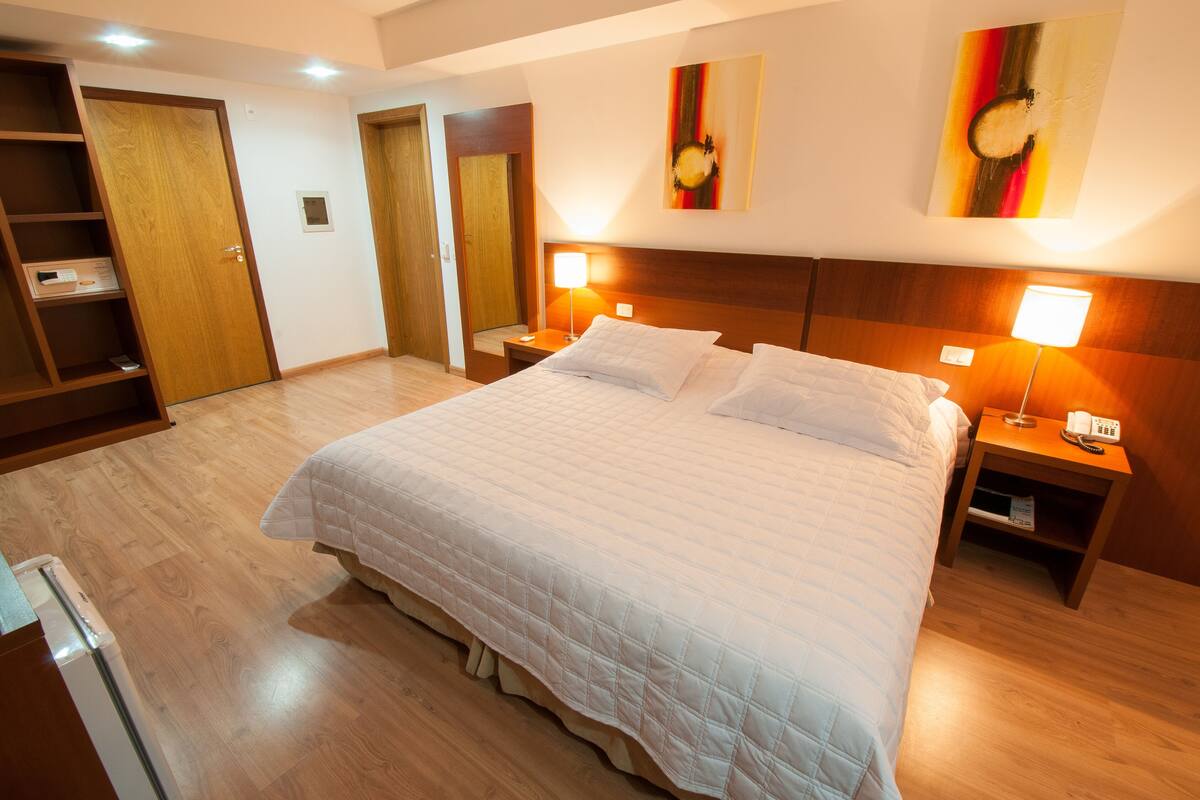 Una habitación de hotel con una cama grande, suelo de madera, un armario y dos lámparas de noche.