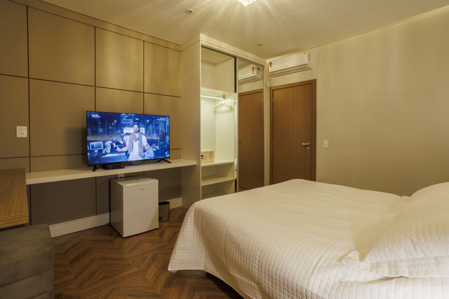 Una habitación de hotel con una cama, televisión, mini refrigerador y armario.