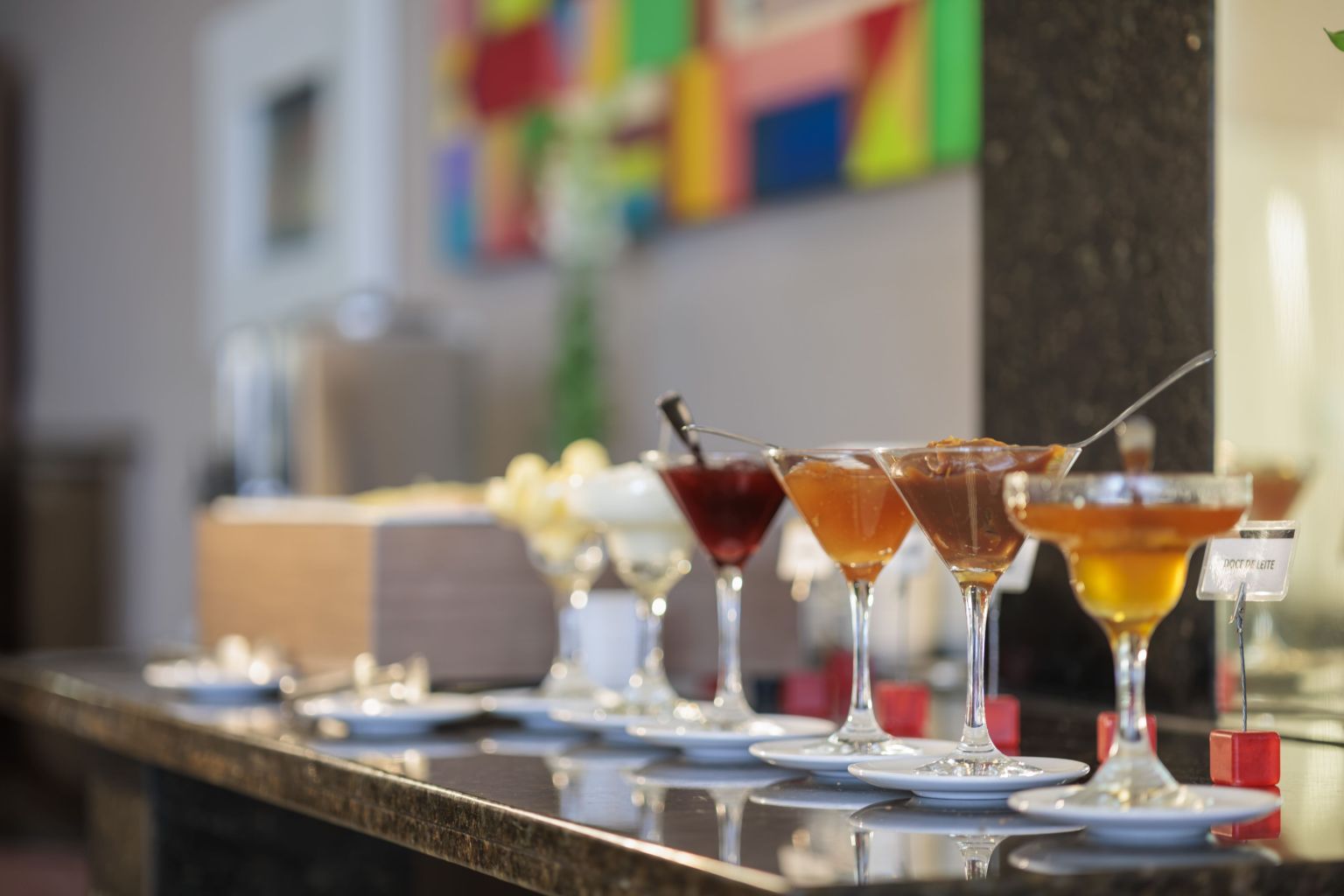 A bar area with multiple glasses of various beverages, a bottle of liquor, and a menu stand.
