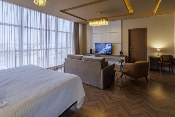 Una habitación de hotel con una cama grande, un sofá, un escritorio con televisor y una silla.