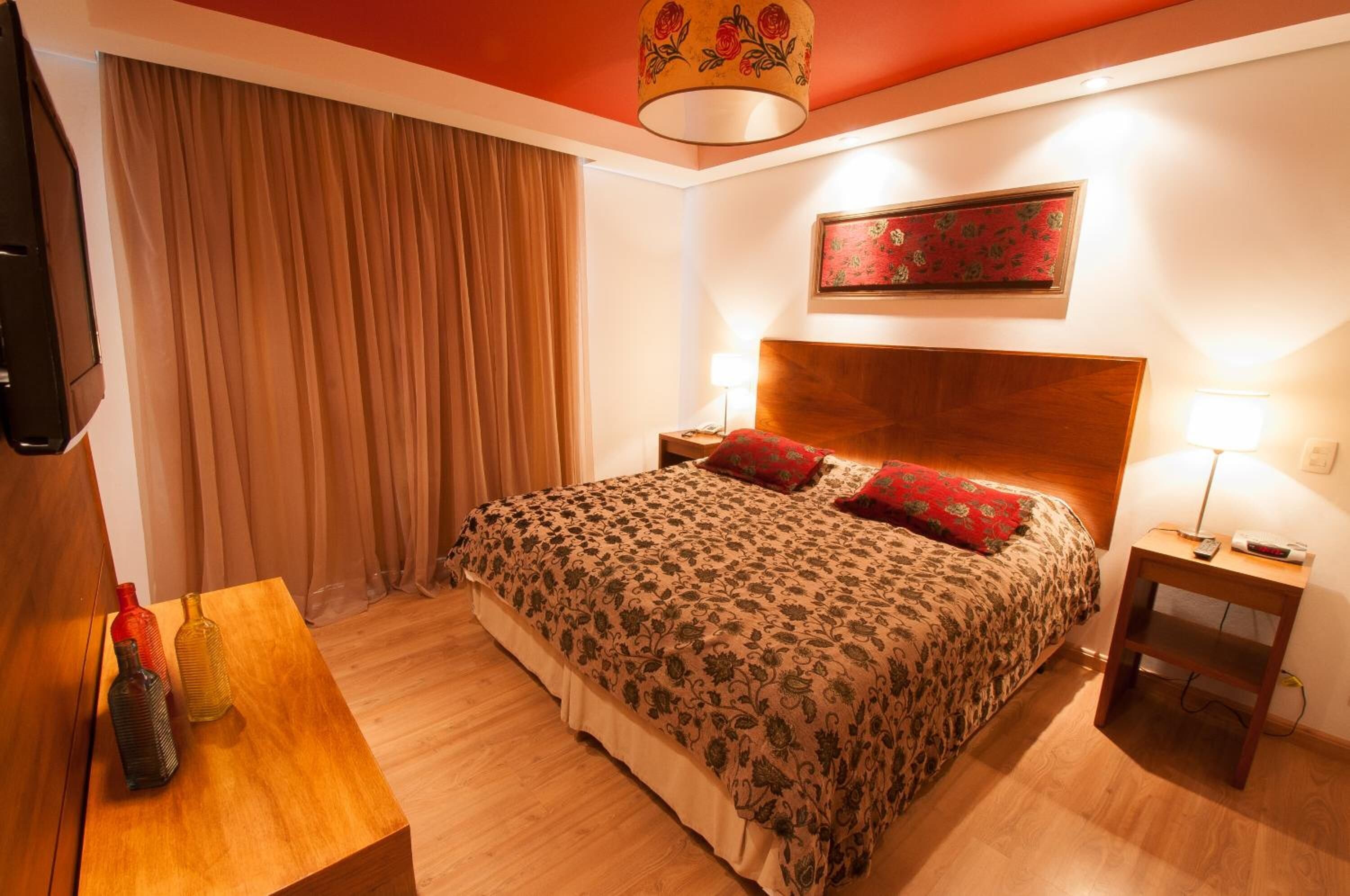 A hotel room with a bed, a nightstand, a lamp, a TV, and a curtain.