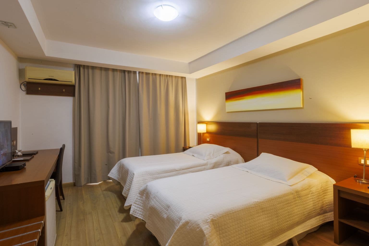 A hotel room with two beds, a desk, and a television.