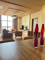 A modern living room with a wooden dining table, two sofas, and a TV in the background.