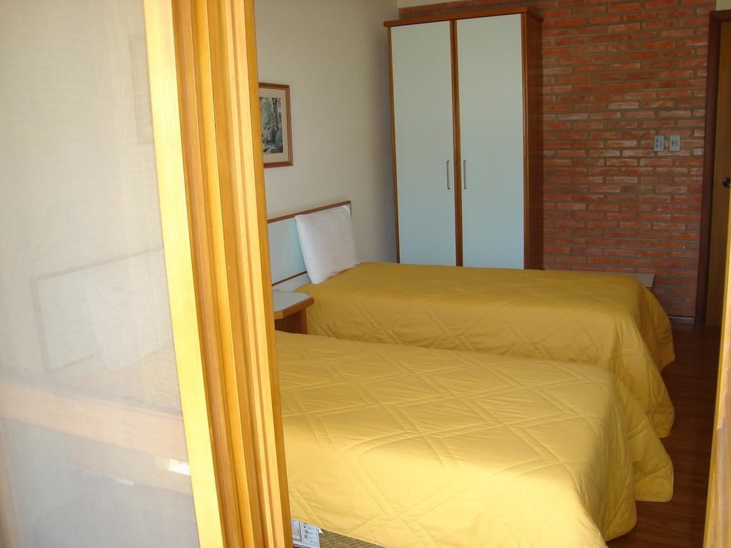 A room with two beds, a wooden wardrobe, and a brick wall.
