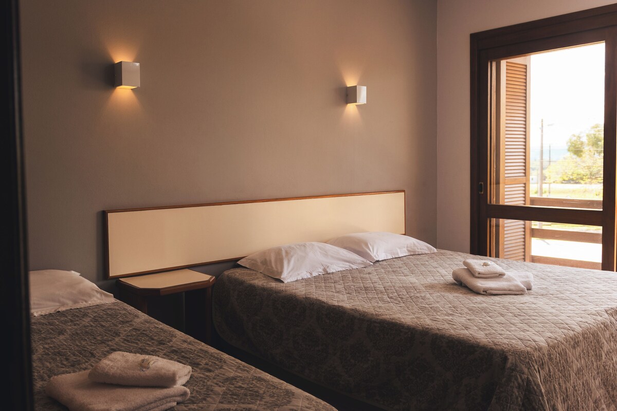 A hotel room with two beds, a nightstand, and a window with blinds.
