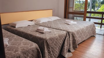 A hotel room with two beds, each with a quilted bedspread and pillows, and a large window offering a view of trees.