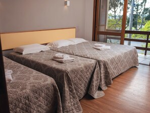 A hotel room with two beds, each with a quilted bedspread and pillows, and a large window offering a view of trees. - Sítio Hotel e Eventos (Sao Pedro do Sul)